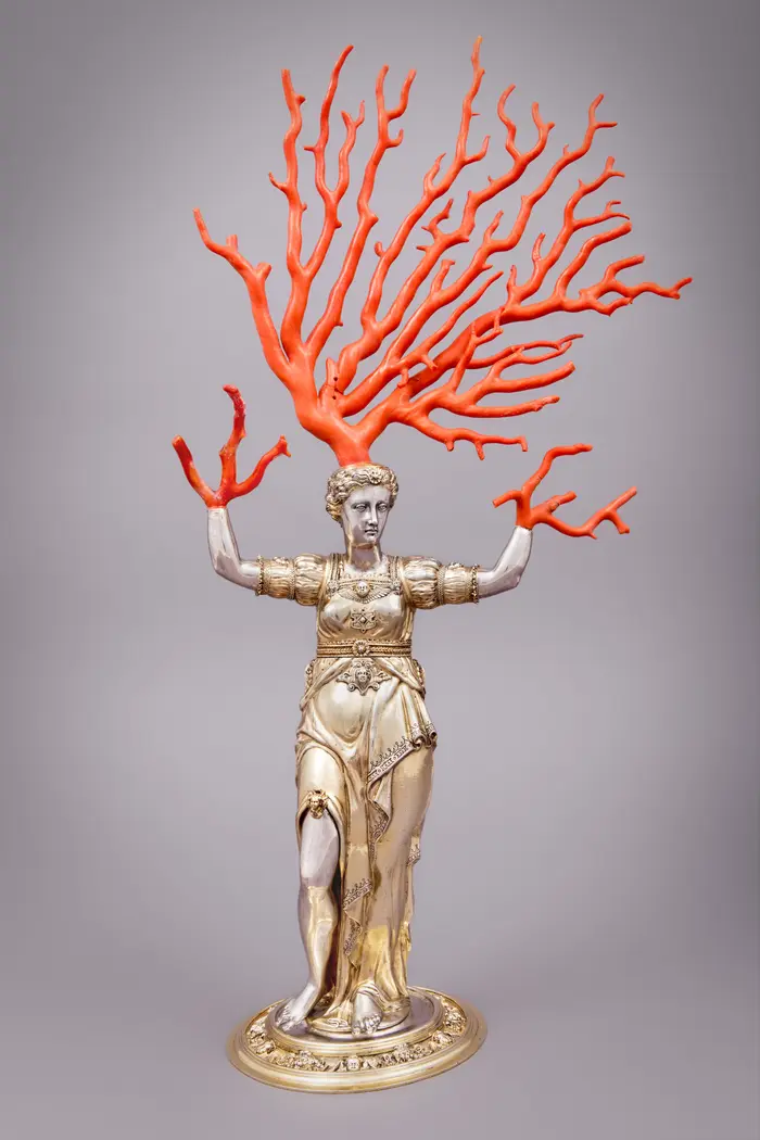 Ein silbergeschmiedeter Pokal in Form der mythologischen Figur der Daphne ist erweitert durch auffächernde, rote Korallenzinken, die die Arme der Figur darstellen.