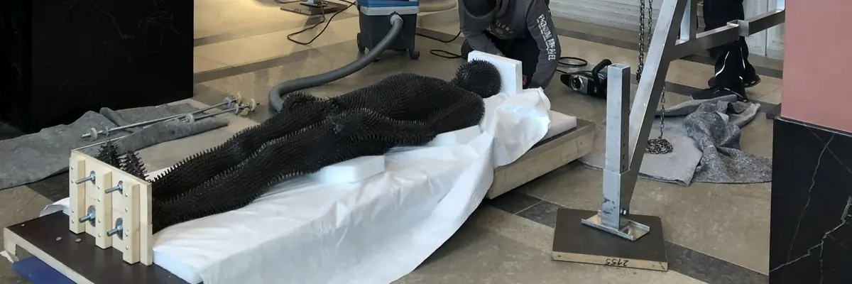 Zu sehen ist das Werk "Under my Skin" von Antony Gormley aus dem Jahr 1997, einem in Eisen ausgeführten einstigen Abgusses des Künstlers. Es ist gänzlich von stacheligen Eisenstiften überzogen. Auf dem Foto wird es liegend vorbereitet um in der antikenhalle installiert zu werden.