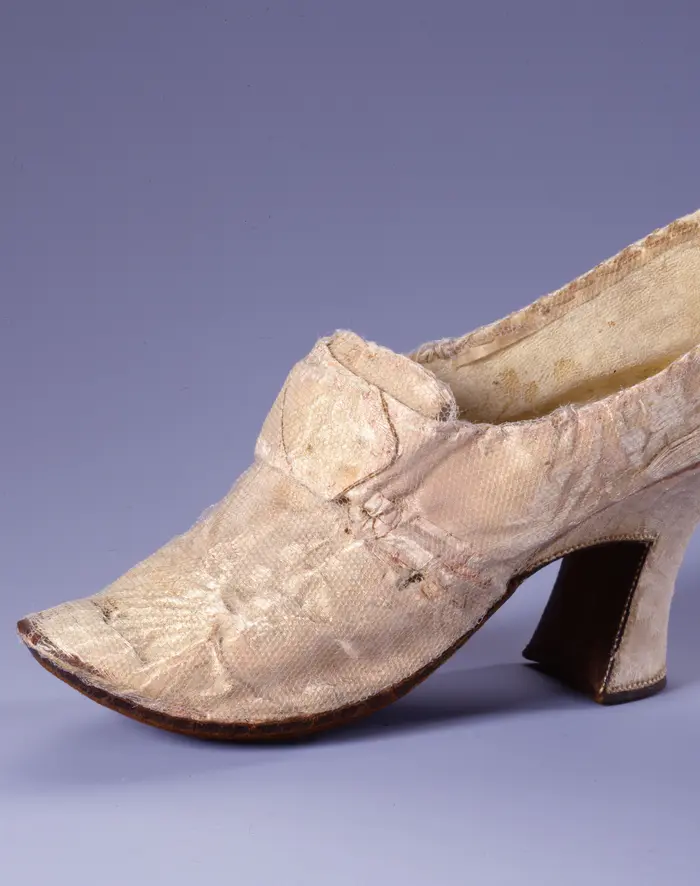 Zu sehen ist ein Tanzschuh aus zartrosa Damastseide mit Absatz. 