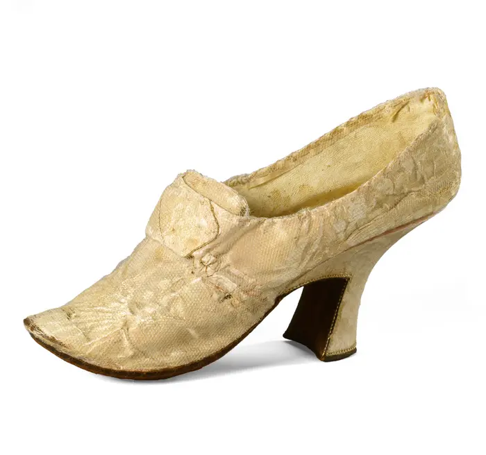 Zu sehen ist ein Tanzschuh aus zartrosa Damastseide mit Absatz. 