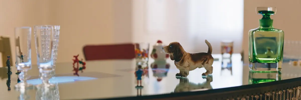 Zu sehen ist eine Detailansicht des Werks von Pipilotti Rist, bestehend aus einem Glastisch mit einer Hundefigur, einem grünen Fläschchen, Gläsern usw.