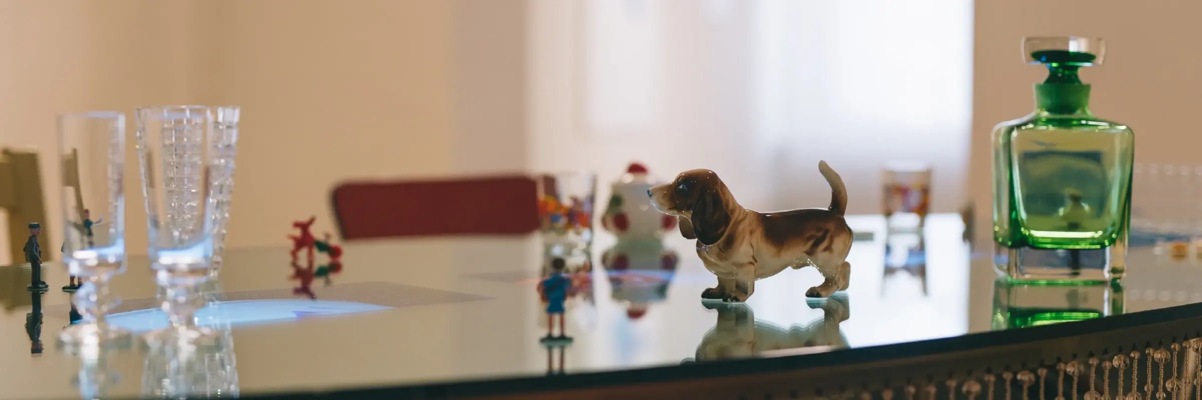 Zu sehen ist eine Detailansicht des Werks von Pipilotti Rist, bestehend aus einem Glastisch mit einer Hundefigur, einem grünen Fläschchen, Gläsern usw.
