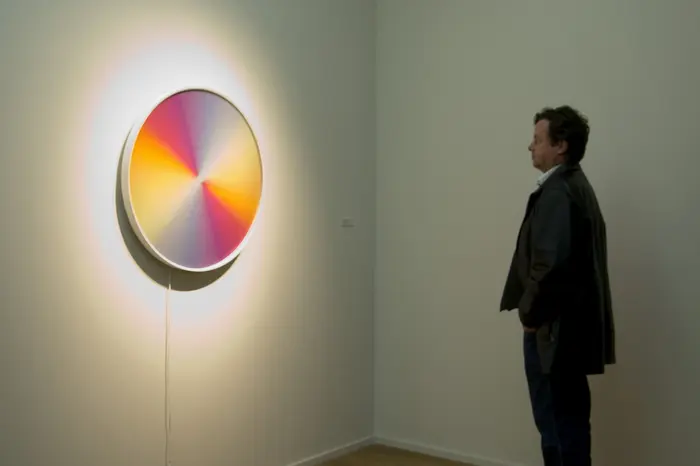 Raumansicht einer Person, die sich ein buntes, rundes Kunstwerk an der Wand anschaut