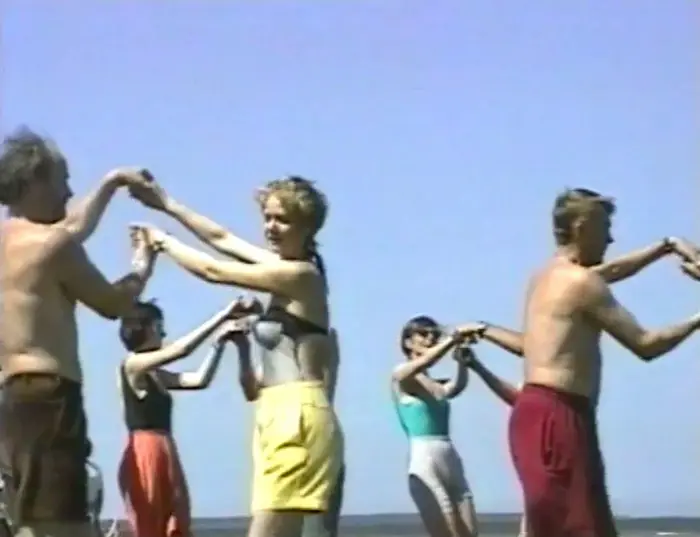Menschen in Freizeitkleidung drehen sich im Paartanz am Strand. 