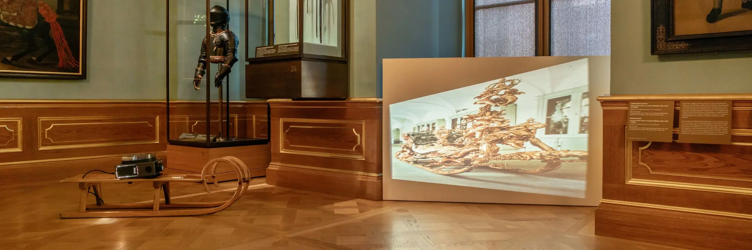 In einem der Paradeappartements steht ein Diaprojektor auf einem herkömmlichen hölzernen Schlitten. Es wird ein Abbild des zeremoniellen Prunkschlittens von König Ludwig II. von Bayern in verzerrter Weise an die Wand projiziert. 