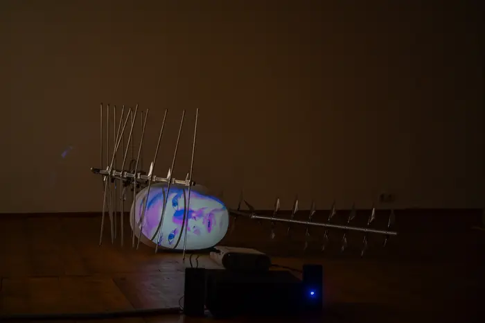 Tony Oursler, "Luftmetall", 2002 Eine Videoskulptur des Künstlers Tony Oursler bestehend aus einem metallenen Empfänger und einer auf dem Boden liegenden Projektionsfläche in Form eines Kopfes, der einen theatralen Monolog hält.