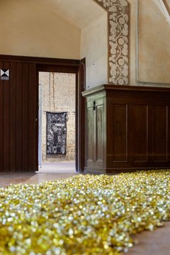Zu sehen ist ein langer Teppich aus goldenen Bonbons auf dem Boden des Ausstellungsrraumes.