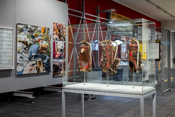 Das Bild zeigt eine an ein Depot angelehnte Ausstellungsarchitektur mit Werken der Schenkung Sammlung Hoffmann, des Kunstfonds, des Kupferstich-Kabinetts und des Albertinums. Auf dem Bild sind „Restrisiko“ von Peter Bux, „Untitled 9 (my name is nobody)“ von Joep van Liefland, „Trash 1“ von Eberhard Havekost, sowie drei Werke aus der Serie „Pflege: Zwischen Zwangshandlung und kultureller Heldentat“ von Janet Grau zu sehen.