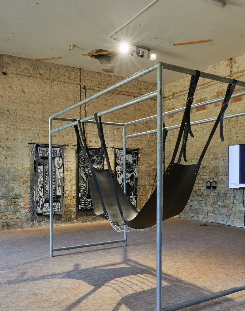 Zu sehen ist eine an BDSM-Ästhetik angelehnte Schaukel von Monica Bonvicini, im Hintergrund ist u.a. ein dreiteiliges Werk von Anja Kaiser zu sehen.