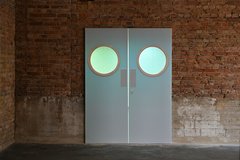 Die Videoprojektion der Künstlerin A K Dolven wirft das Bild zweier realgroßer Türen auf eine Ziegelwand. Die Türen schwingen leicht auf und wieder zu. 