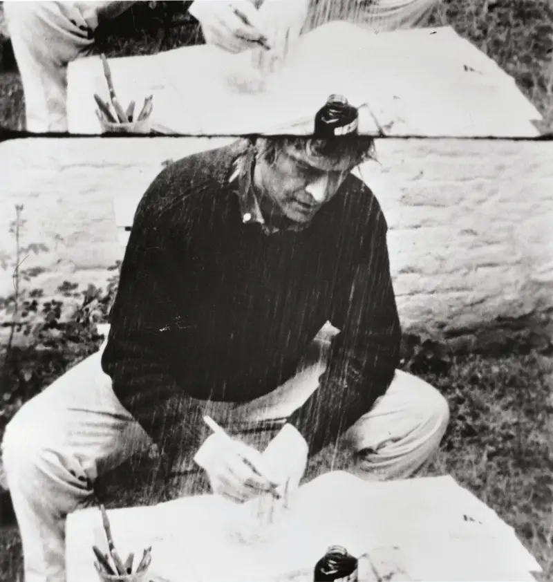 In der Videoarbeit versucht ein Künstler versucht zu zeichnen, während es unentwegt über ihn hinabregnet.