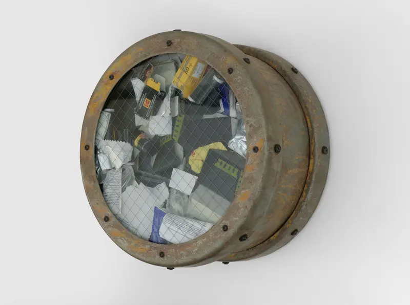 Die Wandinstallation "Catalog: Terra Firma Nineteen Hundred Eighty Nine, #3" aus dem Jahr 1989 von Ashley Bickerton besteht aus zwölf symmetrisch gehangen Bullaugen, die mit unterschiedlichsten Materialien wie Erdnussflips, Zigarettenstummel, Flechten und Korallen gefüllt sind. Auf dem Foto ist ein Detail des mit Fotofilmen gefüllten Behältnisses zu sehen.