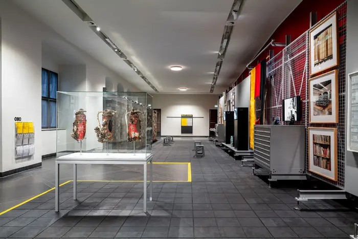 Das Bild zeigt eine an ein Depot angelehnte Ausstellungsarchitektur mit Werken der Schenkung Sammlung Hoffmann, des Kunstfonds, des Kupferstich-Kabinetts und des Albertinums. Die Ausstellungsansicht ist ein Blick in den Raum und zeigt u.a. Peter Bux‘ „Restrisiko“, sowie drei Fotografien von Candida Höfer rechts an der Wand.