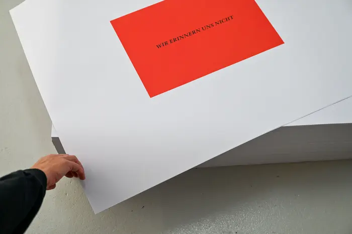 Felix Gonzalez-Torres "Untitled" (We don't remember), 1991 Ein Stapel Poster liegt auf einem Parkettboden, auf weißem Grund ist ein rotes Quadrat gedruckt mit dem Satz "Wir erinnern uns nicht"