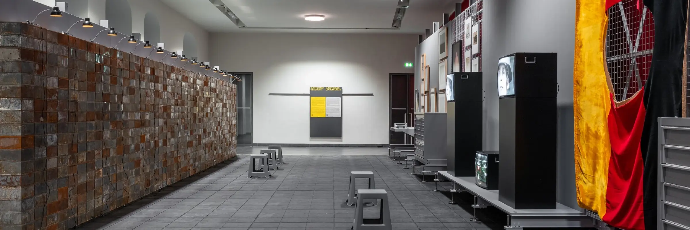 Das Bild zeigt eine an ein Depot angelehnte Ausstellungsarchitektur mit Werken der Schenkung Sammlung Hoffmann, des Kunstfonds, des Kupferstich-Kabinetts und des Albertinums. Das Bild zeigt einen Blick in den Ausstellungsraum, unter anderem sind Werke von Christian Boltanski, Georg Herold oder Marcel Odenbach zu sehen. 