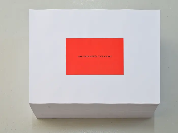 Felix Gonzalez-Torres "Untitled" (We don't remember), 1991 Ein Stapel Poster liegt auf einem Parkettboden, auf weißem Grund ist ein rotes Quadrat gedruckt mit dem Satz "Wir erinnern uns nicht"