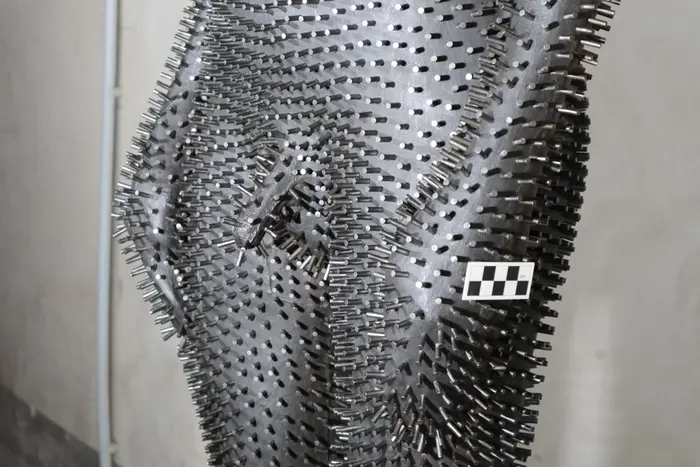 Zu sehen ist das Werk "Under my Skin" von Antony Gormley aus dem Jahr 1997, einem in Eisen ausgeführten einstigen Abgusses des Künstlers. Es ist gänzlich von stacheligen Eisenstiften überzogen. Auf dem Foto wird es liegend vorbereitet um in der Antikenhalle installiert zu werden.