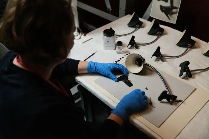 Das Bild zeigt die Restauratorin Franziska Klinkmüller im blauen Gummihandschuhen bei der Arbeit an den Leuchten des Werks Christian Boltanskis. 