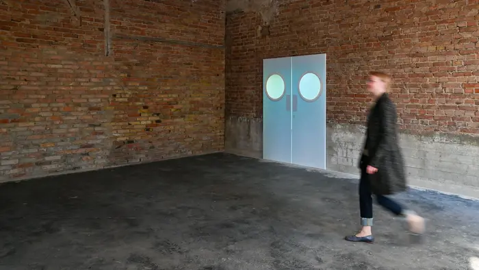 Die Videoprojektion der Künstlerin A K Dolven wirft das Bild zweier realgroßer Türen auf eine Ziegelwand. Die Türen schwingen leicht auf und wieder zu. 